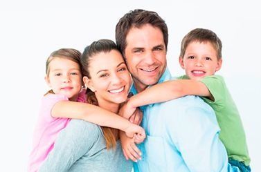 Familia sonriente de cuatro personas abrazándose fuertemente sobre un fondo blanco.