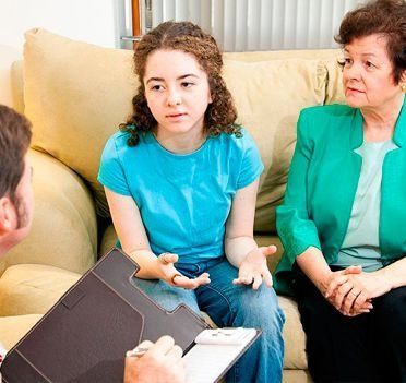 Una joven y una consejera conversan sentadas en un sofá, mientras otra mujer escucha a su lado.
