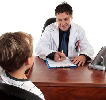 Un médico habla con un paciente al otro lado de un escritorio y toma notas en el consultorio de la clínica.