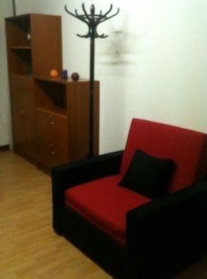 Un sillón rojo y negro en una habitación con una estantería de madera y un perchero.