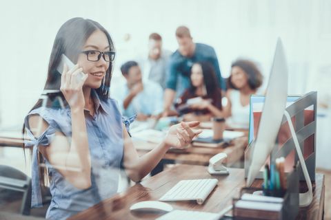 Una mujer está sentada en un escritorio frente a una computadora hablando por un teléfono celular.