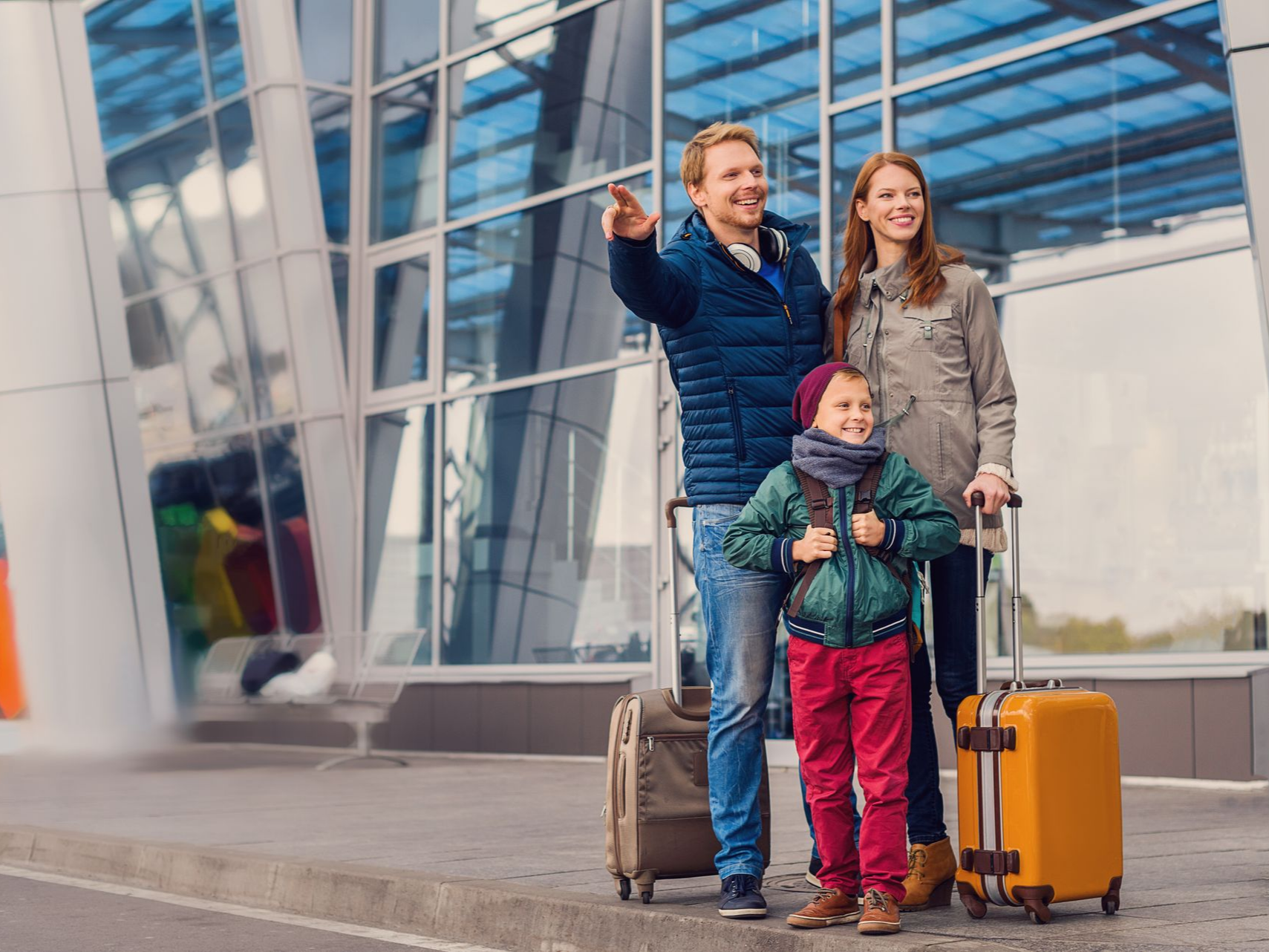 Une famille avec des bagages fait un signe du doigt devant l'aéroport.