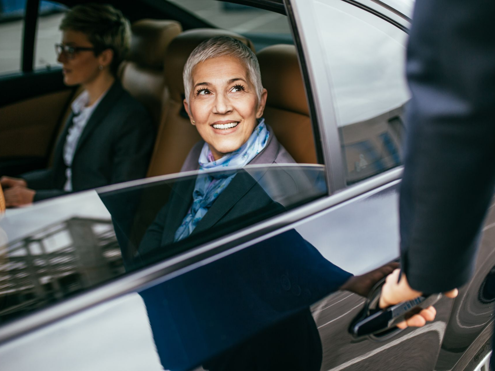 Une femme sourit en sortant d'une voiture ; le préposé lui ouvre la portière.