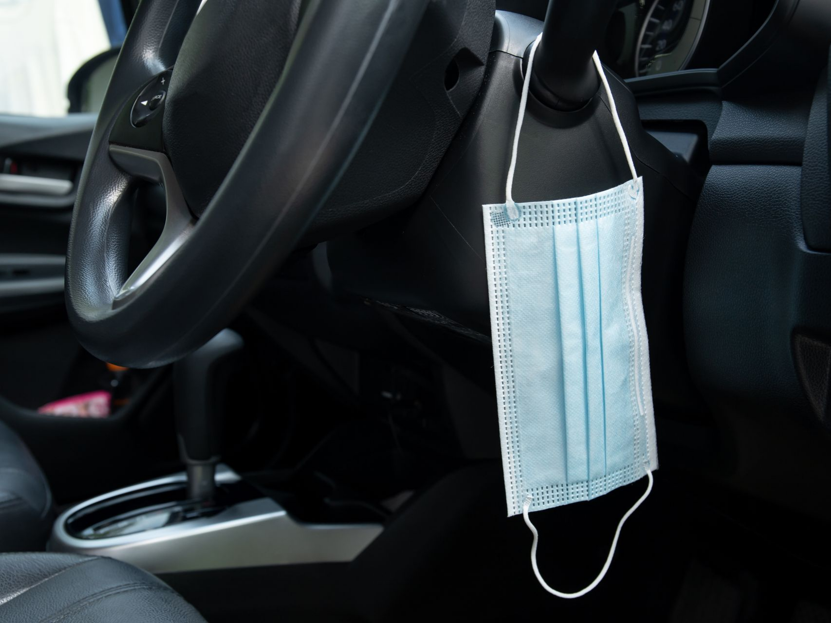 Un masque bleu est accroché au volant à l'intérieur d'une voiture.
