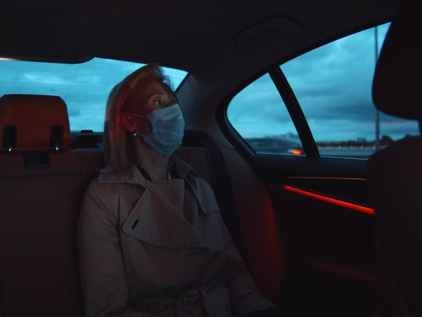 Une femme portant un masque dans une voiture regarde par la fenêtre le crépuscule.