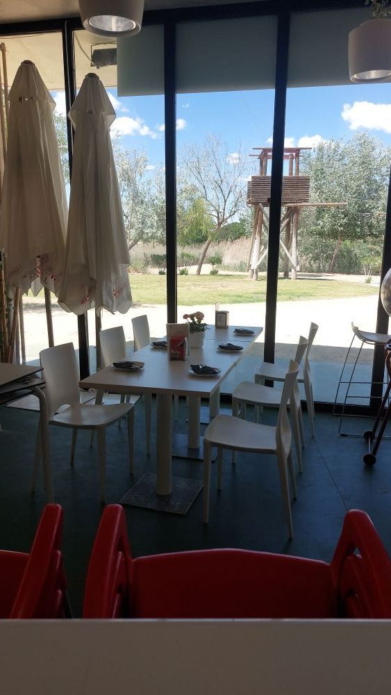 Un restaurante con mesas, sillas y sombrillas frente a un gran ventanal.