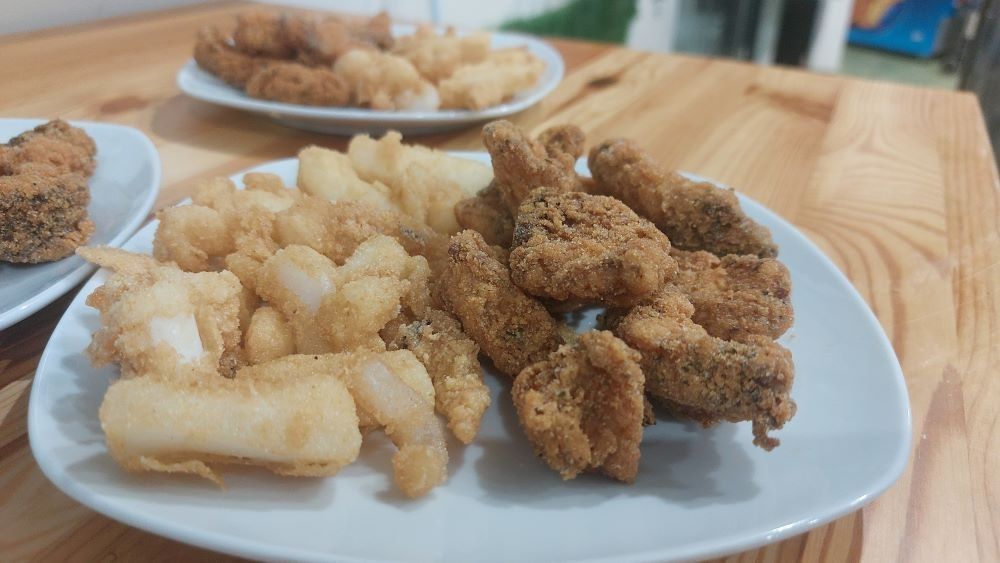 Un plato blanco cubierto con comida frita y papas fritas sobre una mesa de madera.