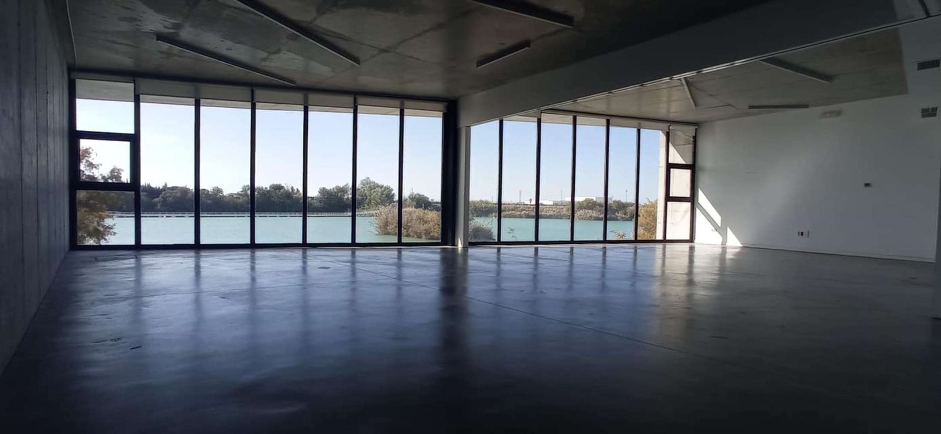 Una gran habitación vacía con muchas ventanas y vista a un lago.