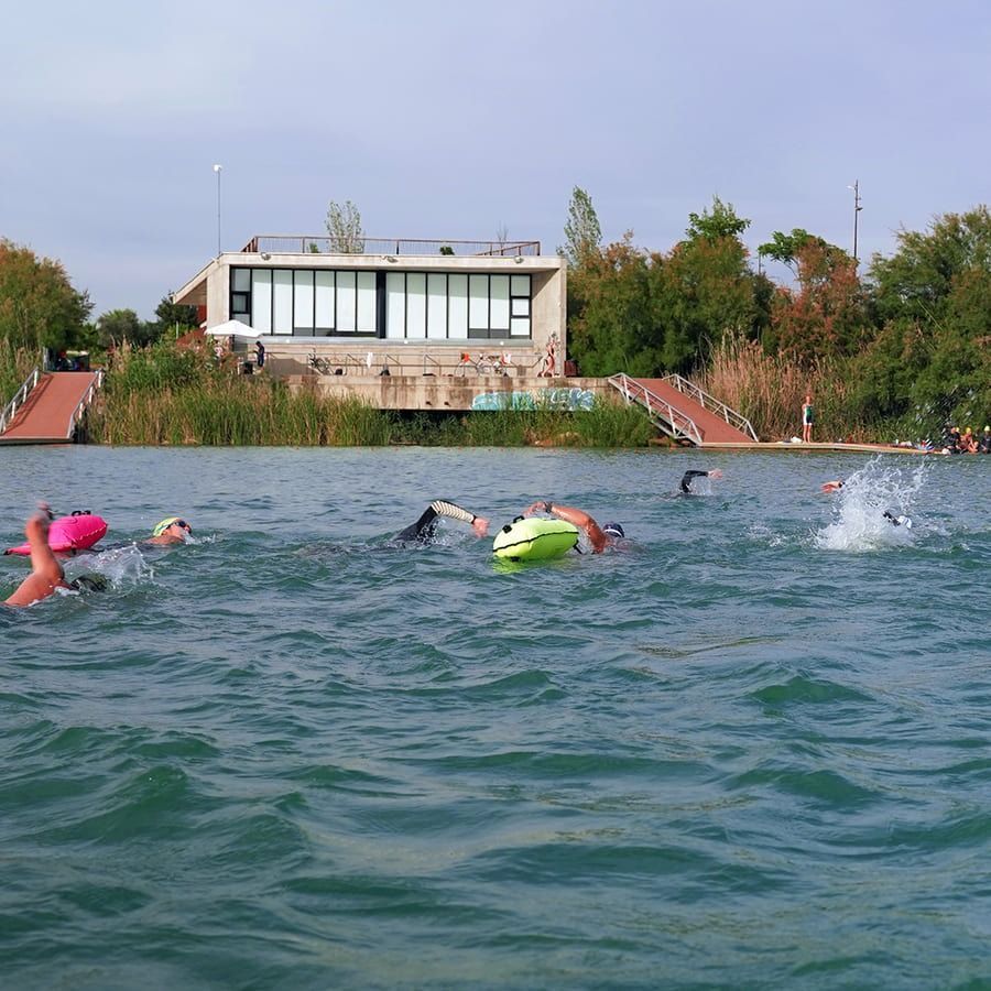 Un grupo de personas está nadando en un lago con un edificio al fondo.