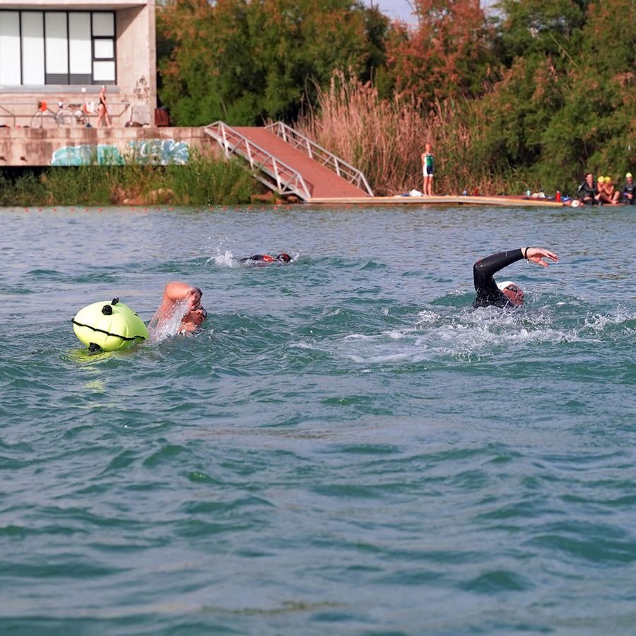 Dos personas están nadando en un lago con una pelota amarilla en el agua.