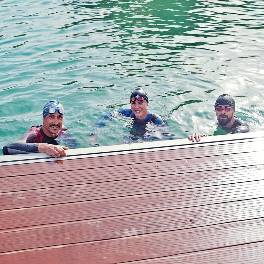 Tres hombres están nadando en un lago y uno está apoyado en una plataforma de madera.
