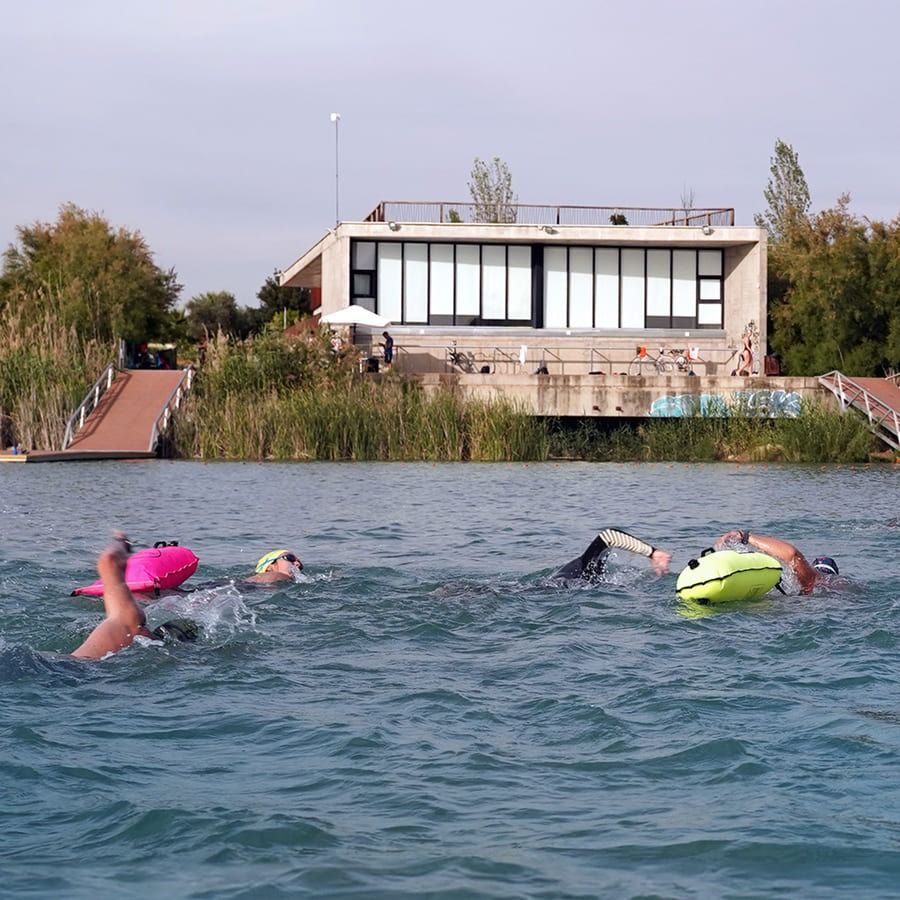 La gente está nadando en un lago con un edificio al fondo.