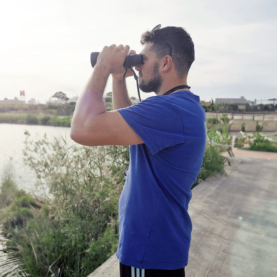 Un hombre con camisa azul mira a través de binoculares.