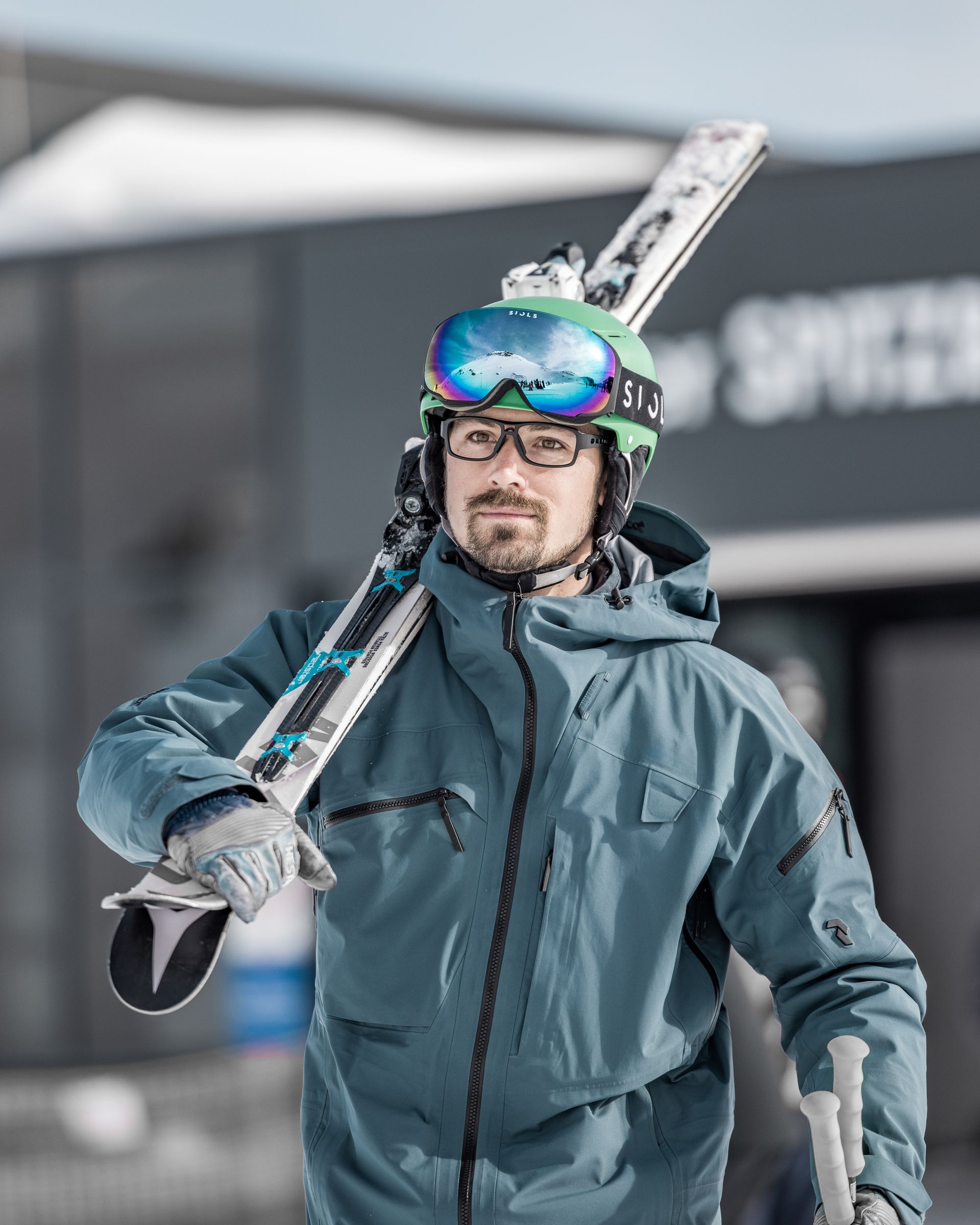 Ein Mann mit Helm und Schutzbrille trägt Skier auf seiner Schulter.