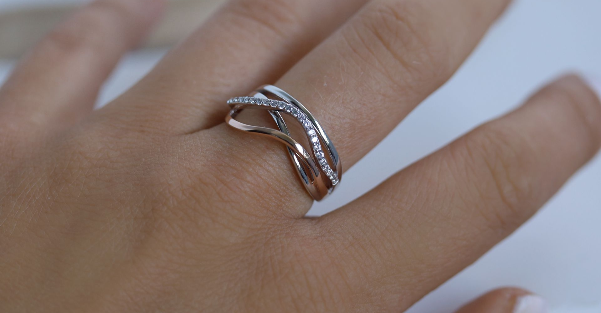 Hand, die einen mehrreihigen Ring mit Diamanten auf einer weißen Oberfläche trägt.