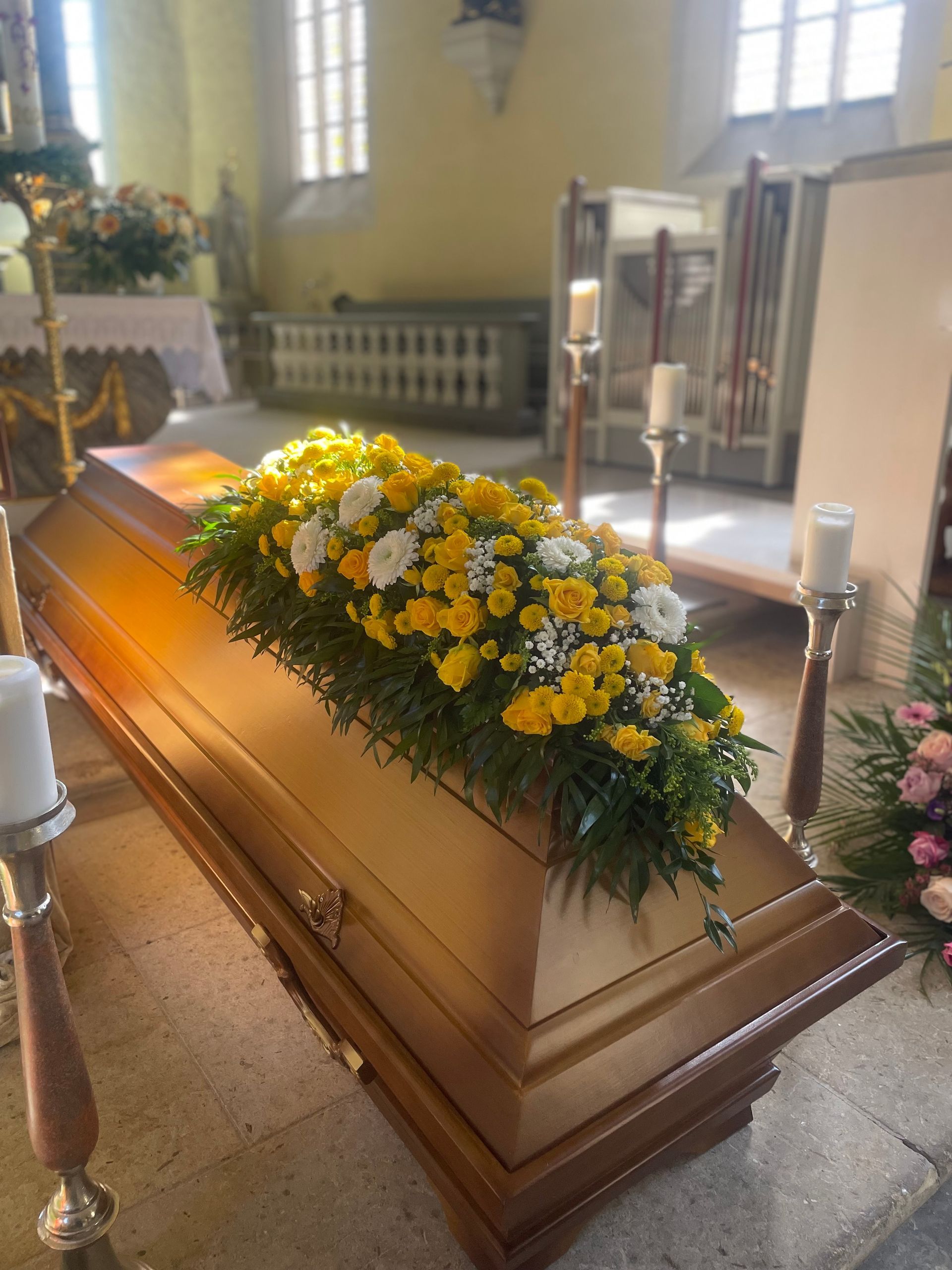 Gelb/weißer Blumenkranz auf dem Sarg