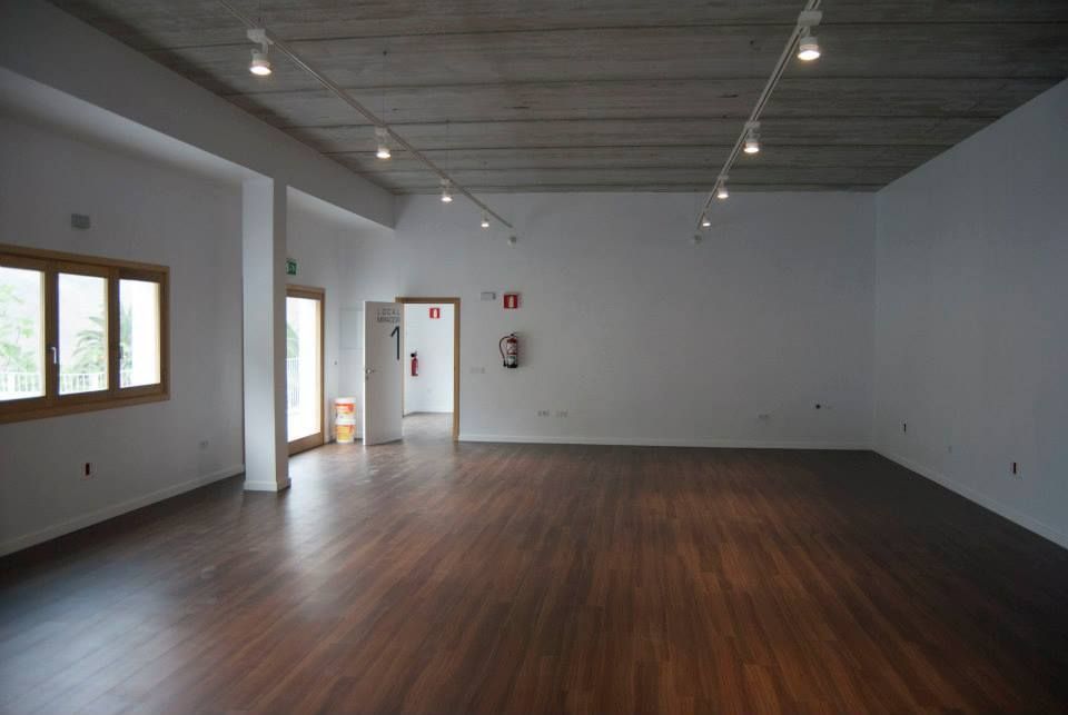 Estudio vacío con suelo de madera, paredes blancas y grandes ventanales a la izquierda.