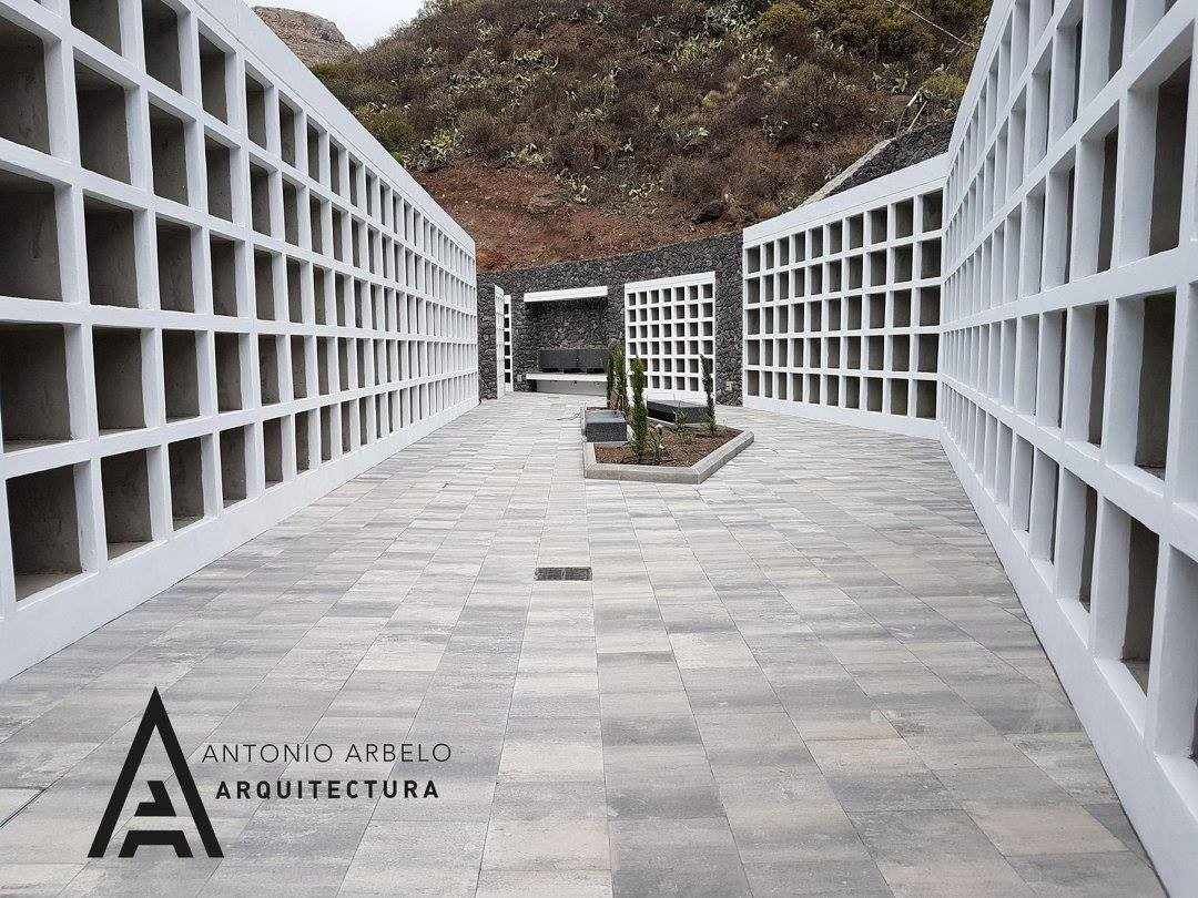 Un moderno sendero de piedra entre muros de rejilla blanca conduce a un pequeño banco y a árboles más allá.