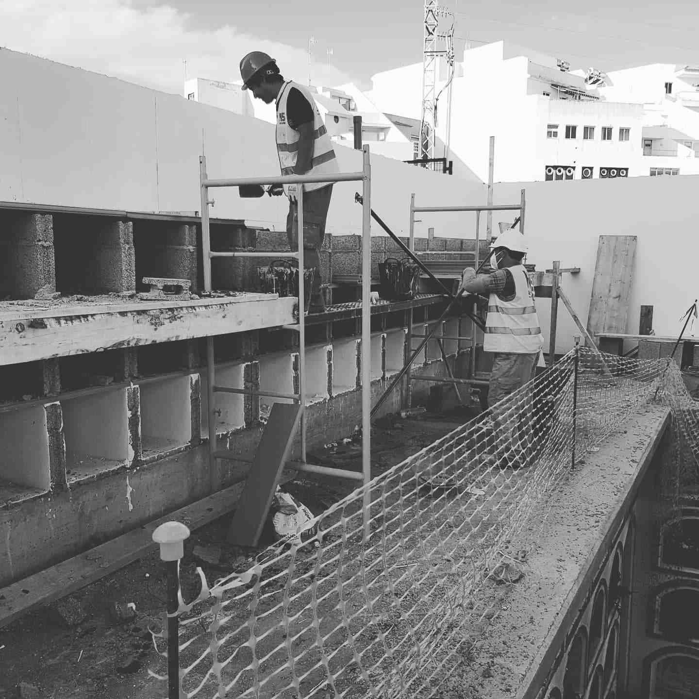 Obrero en un andamio junto a un edificio en construcción, con una red de seguridad en primer plano.