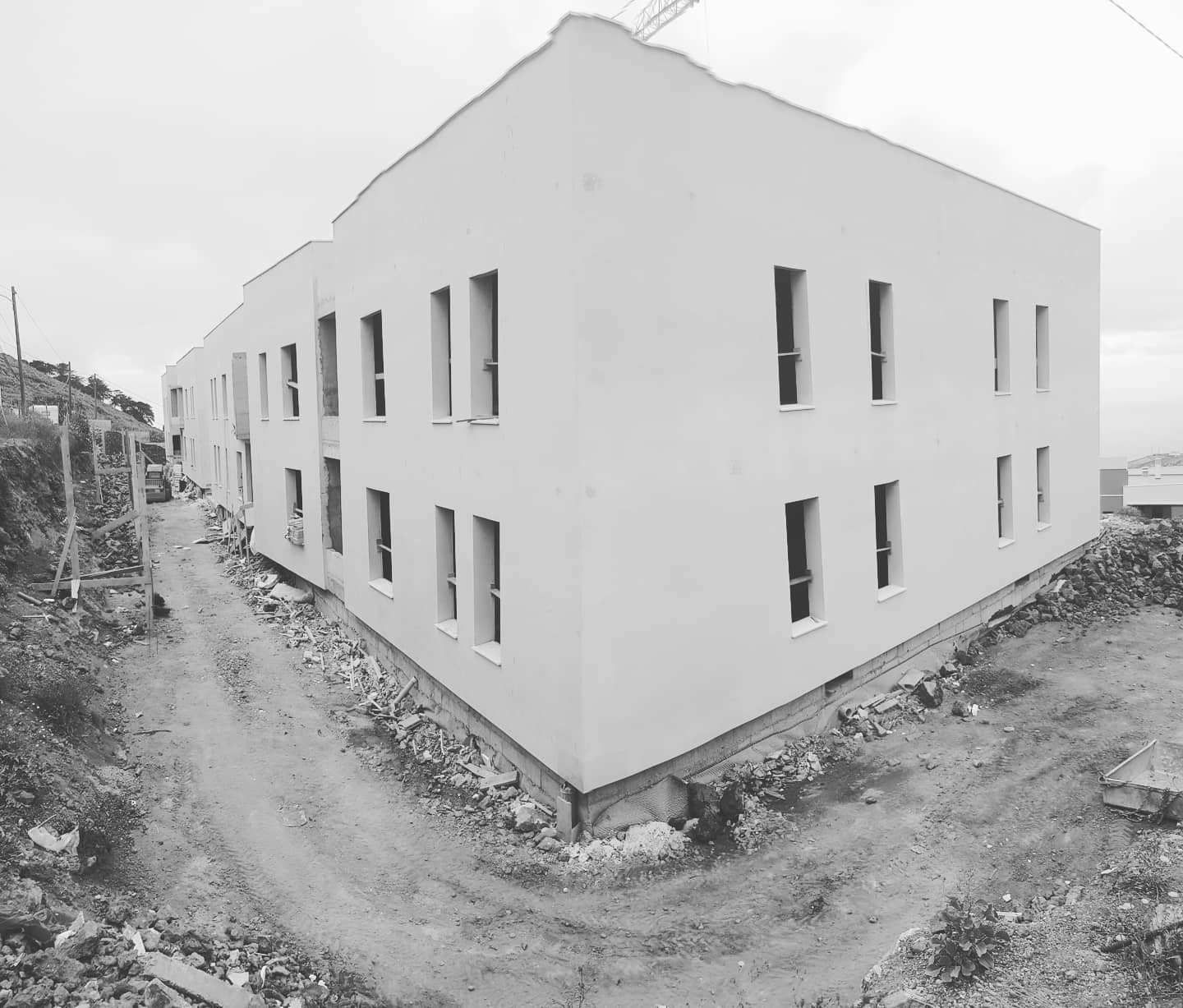 Edificio blanco de dos plantas con ventanas estrechas en un solar de tierra, visto en blanco y negro.