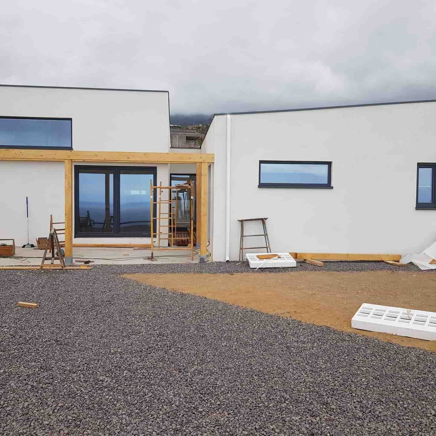 Exterior de una casa moderna en construcción con paredes blancas, ventanas azules y patio de grava.