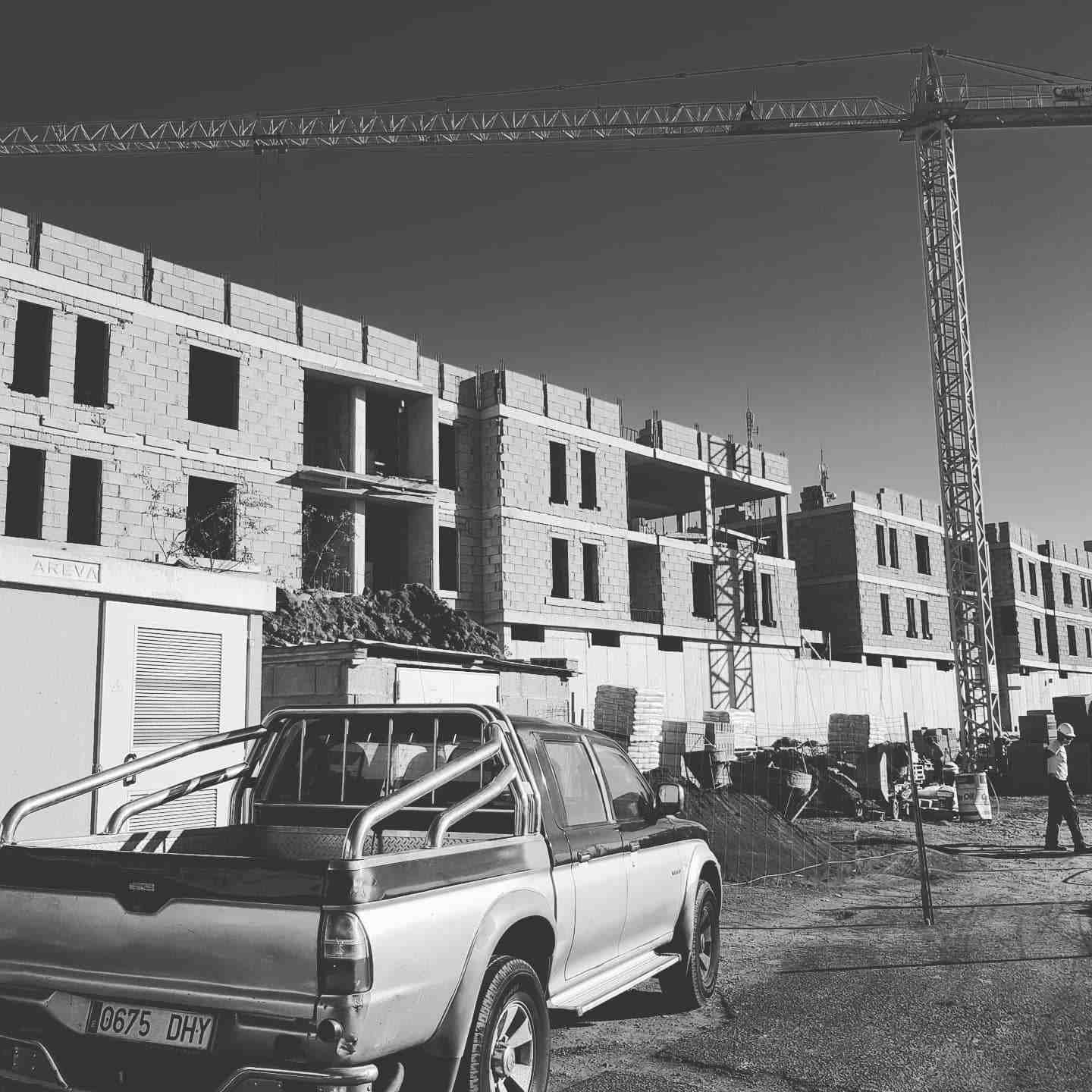 Camioneta estacionada junto a un bloque de apartamentos parcialmente construido con una grúa en lo alto.