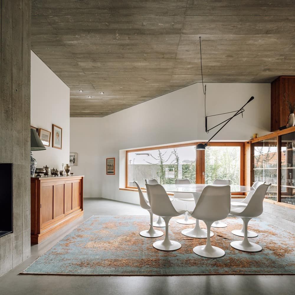 Comedor moderno con sillas blancas, una mesa larga, un gran ventanal y techo de hormigón.