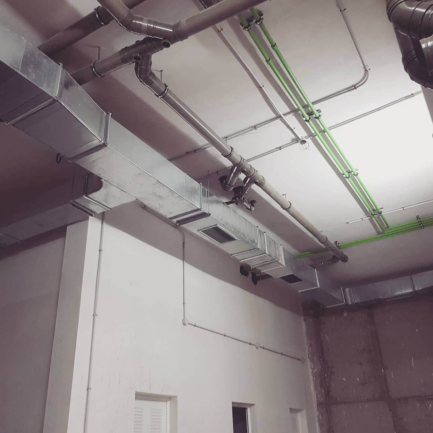 Vista desde el techo de conductos, tuberías y luces fluorescentes expuestas en un interior industrial.