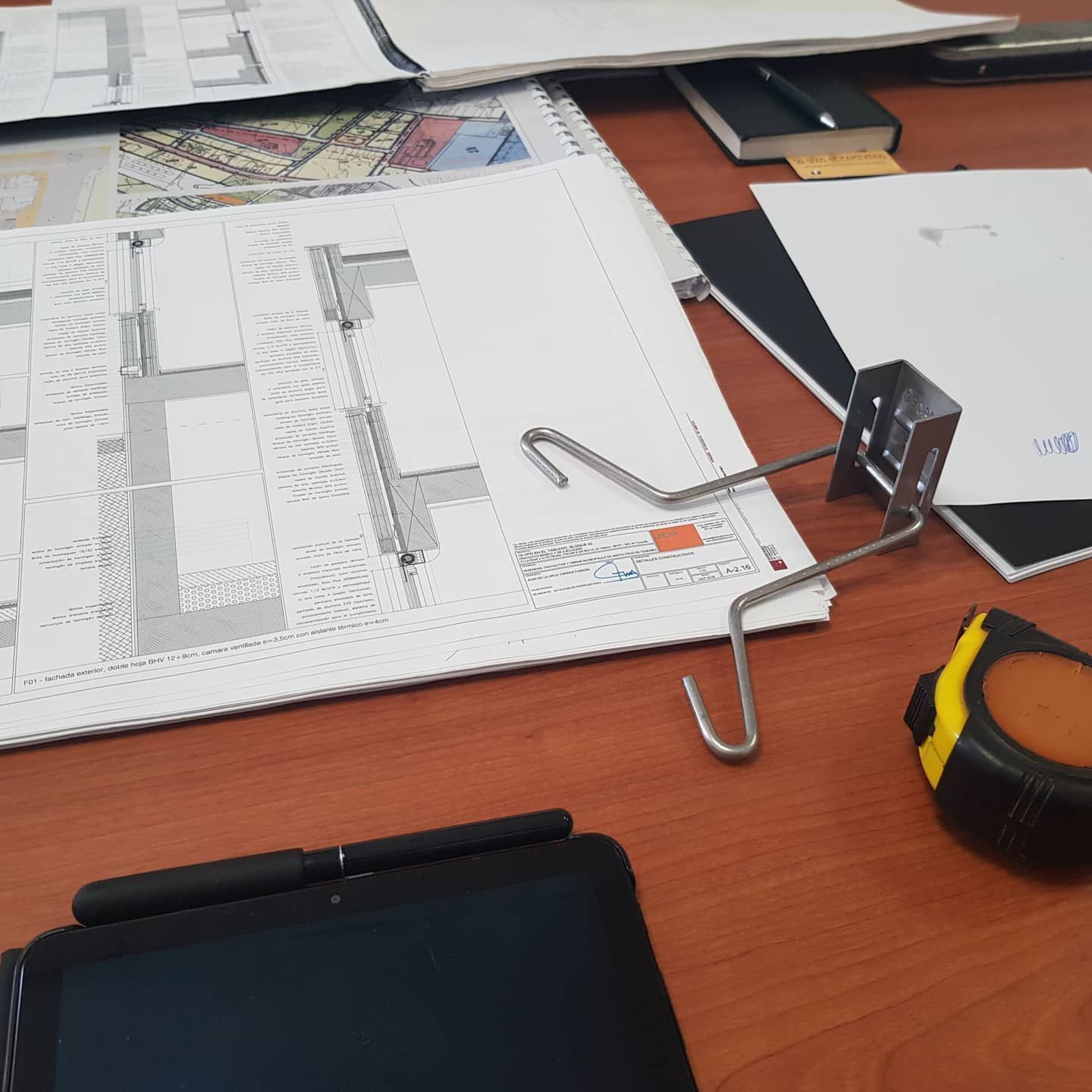 Escritorio con papeles, clips para carpetas y una herramienta de medición sobre una superficie de trabajo de madera.