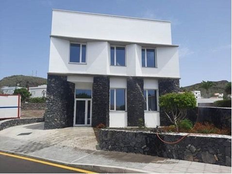 Moderna casa blanca de dos plantas con detalles de piedra oscura y un camino de entrada curvo bajo un cielo despejado.
