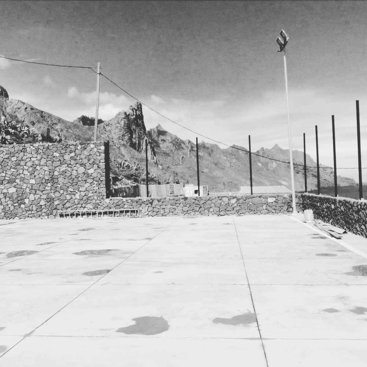 Una cancha de concreto vacía junto a montañas rocosas y altos postes de luz bajo un cielo despejado.