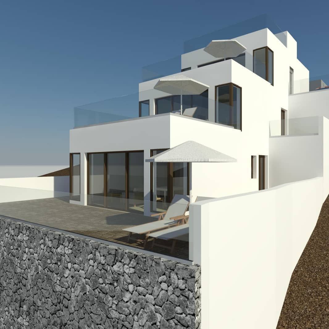 Moderna casa blanca de varias plantas con grandes ventanales, terrazas y un muro de contención de piedra junto al mar.