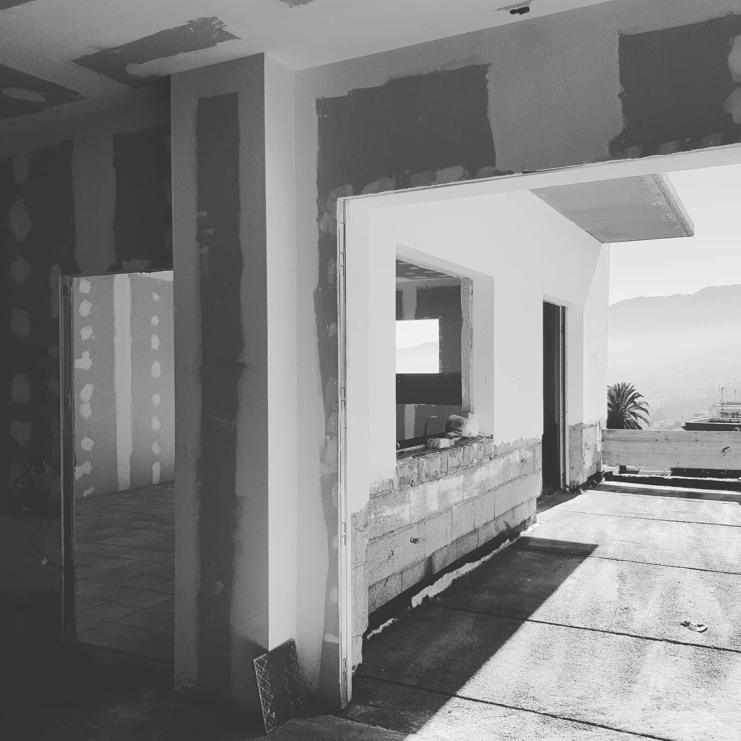 Vista en blanco y negro de un porche moderno con puerta abierta, encimera de piedra y patio luminoso bañado por el sol con vistas al mar.