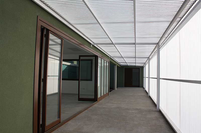Pasillo cubierto y vacío, con puertas de cristal y paneles de pared blancos, que conduce a un final oscuro.