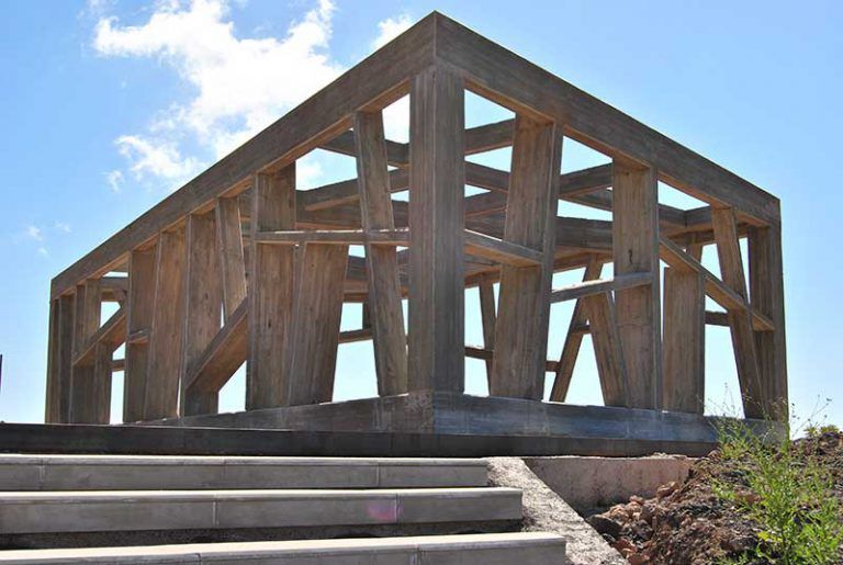 Estructura de madera sobre una base de hormigón, vista desde abajo contra un cielo azul.