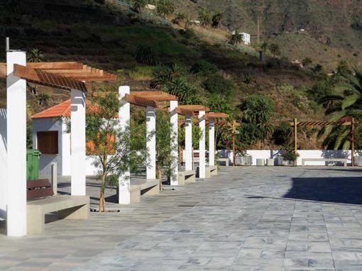 Patio empedrado con columnas blancas y pérgolas naranjas junto a un jardín en la ladera.