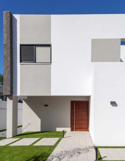 Casa moderna blanca de dos plantas con puerta de entrada de madera, ventanas pequeñas y un camino de césped.