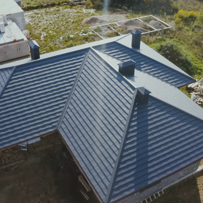 Vue en plongée d'un toit en métal gris avec plusieurs cheminées sur une maison en construction.