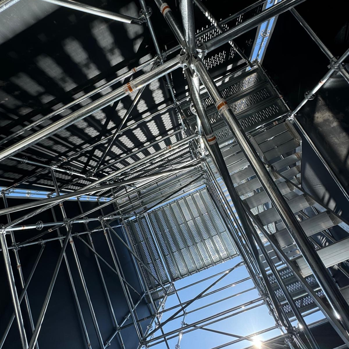 Des ouvriers du bâtiment travaillent sur un échafaudage sur un chantier. L'un monte, l'autre descend.
