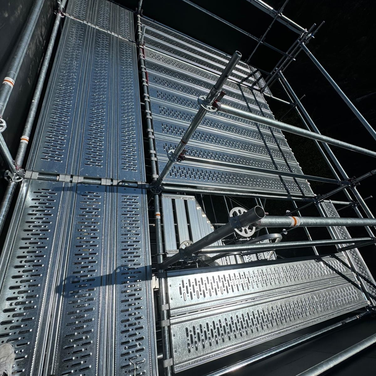 Ouvrier du bâtiment sur une échelle travaillant sur la structure du plafond à l'intérieur d'un bâtiment ; portant un harnais de sécurité et un casque de chantier.