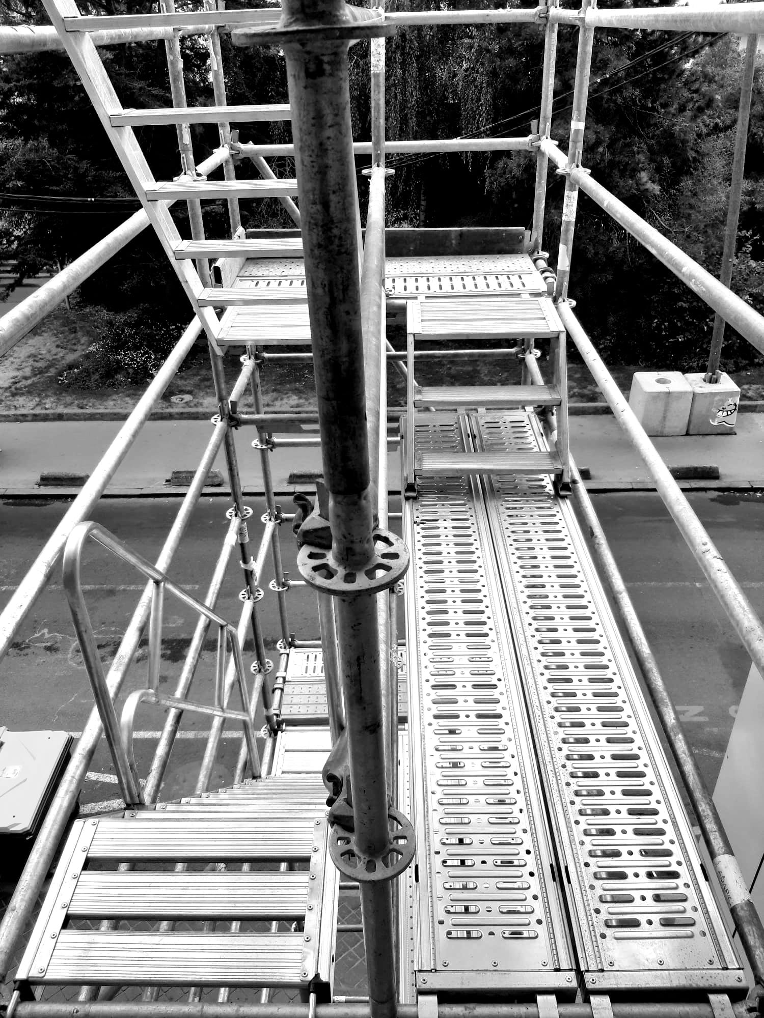 Échafaudage à côté d'un bâtiment au bardage gris foncé et aux panneaux bruns.