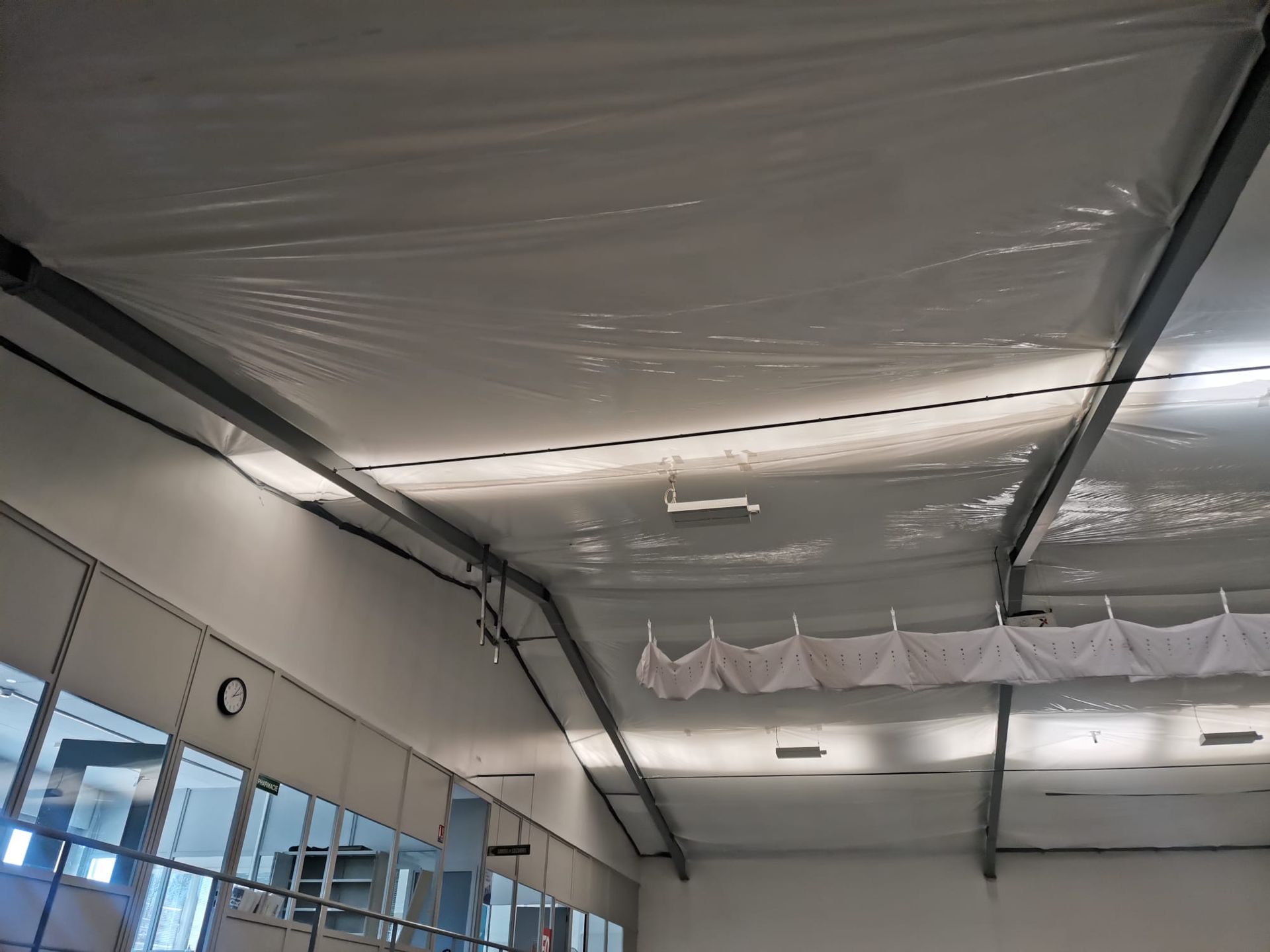 Bâtiment en construction, recouvert d'une bâche de protection blanche, avec des échafaudages se détachant sur un ciel bleu.