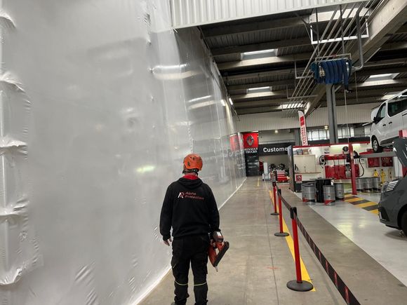 Une personne portant un équipement de sécurité marche dans un couloir d'atelier, en passant devant une barrière en plastique.