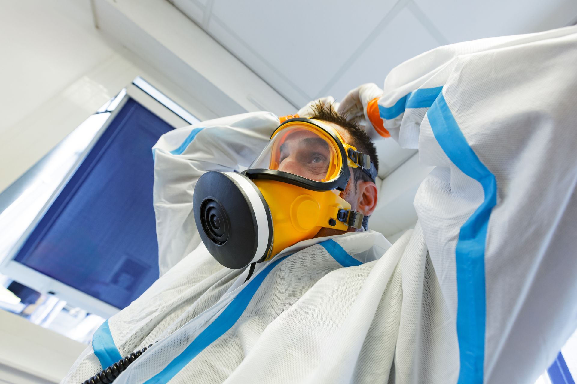 Personne portant un masque à gaz et une combinaison de protection dans un environnement de laboratoire.