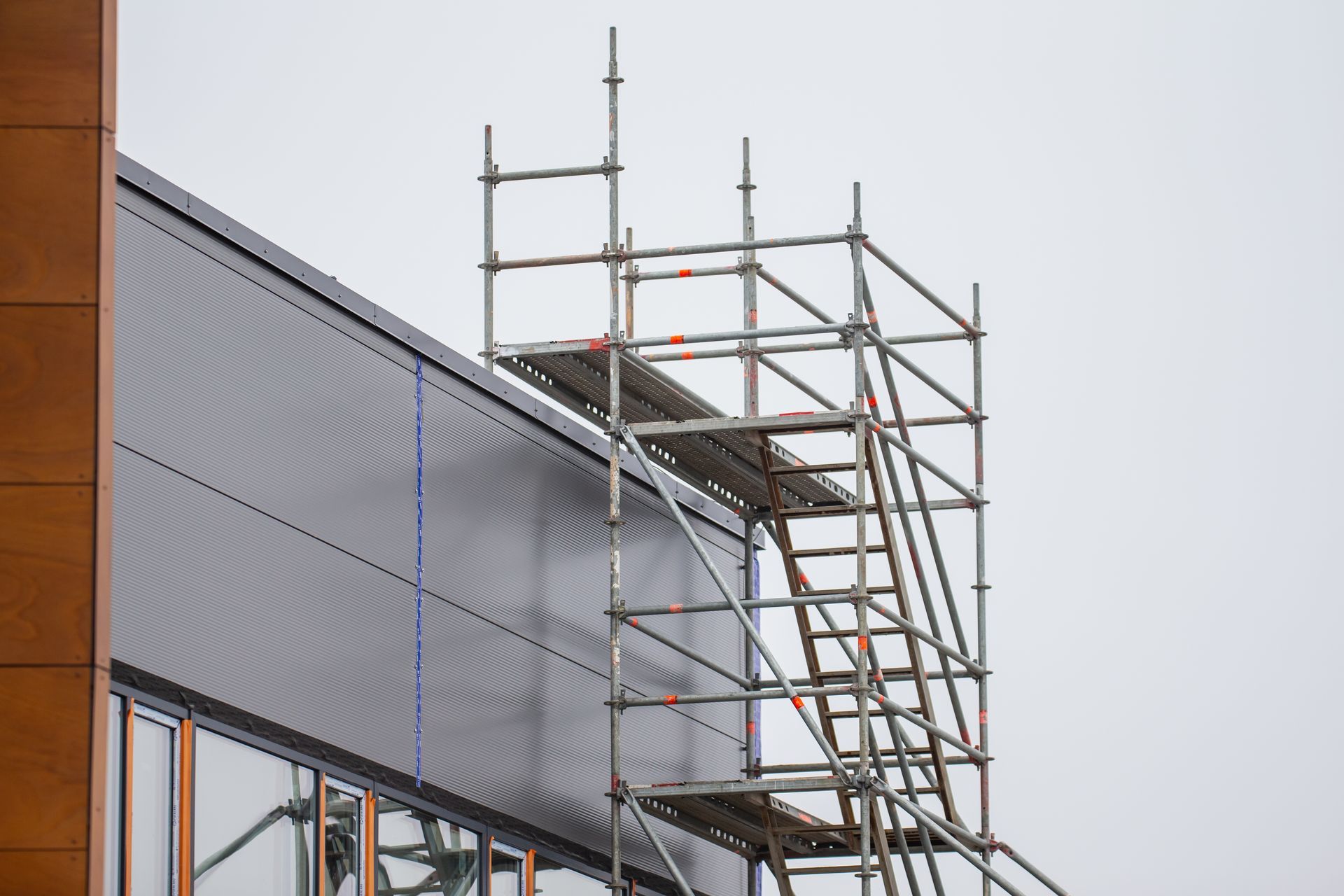 Échafaudage fixé sur le côté d'un bâtiment moderne aux panneaux gris foncé et au bardage en bois brun.