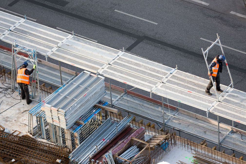 Des ouvriers du bâtiment montent des échafaudages sur un chantier en bordure de route.