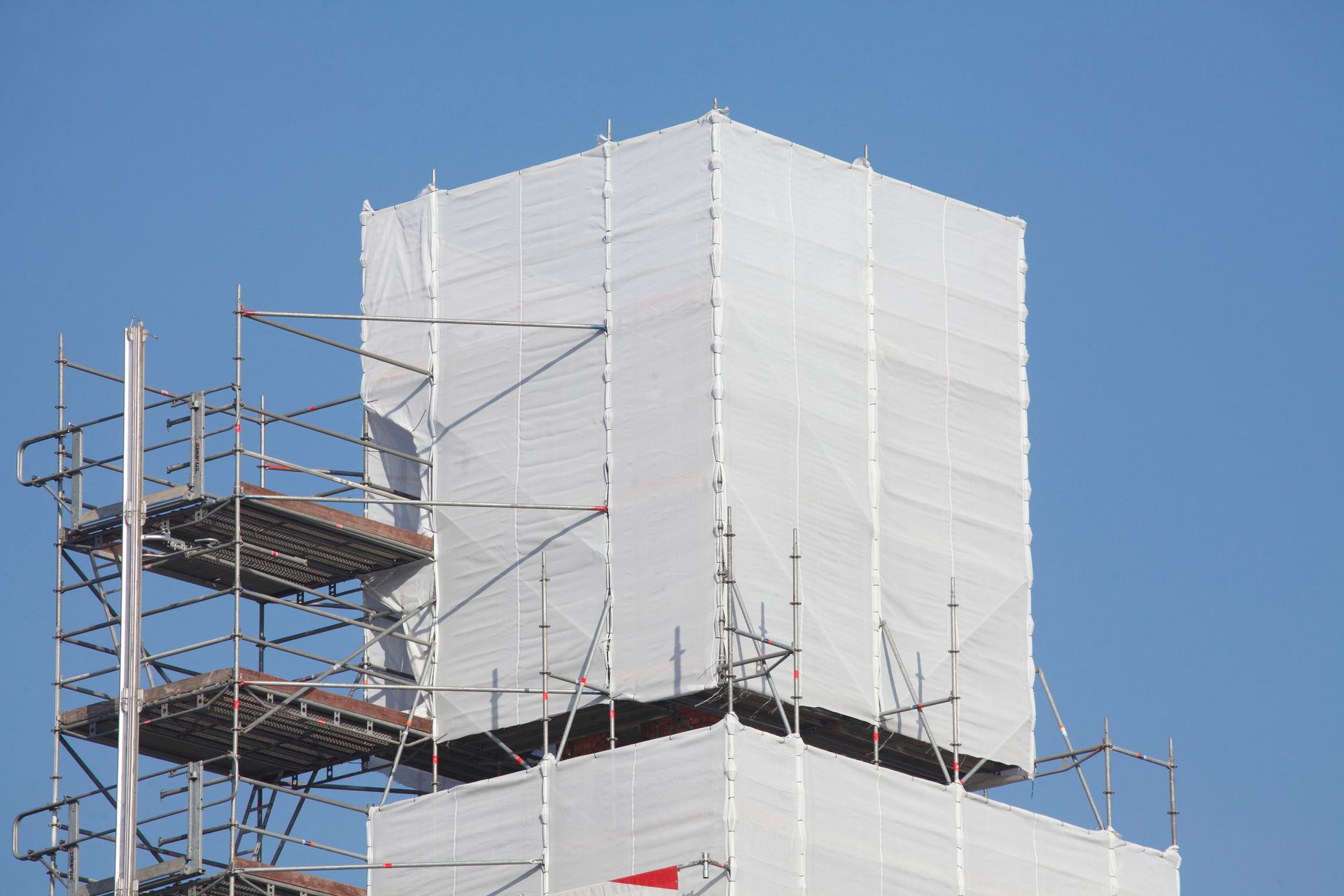 Échafaudages et bâches de protection blanches sur un bâtiment, se détachant sur un ciel bleu.