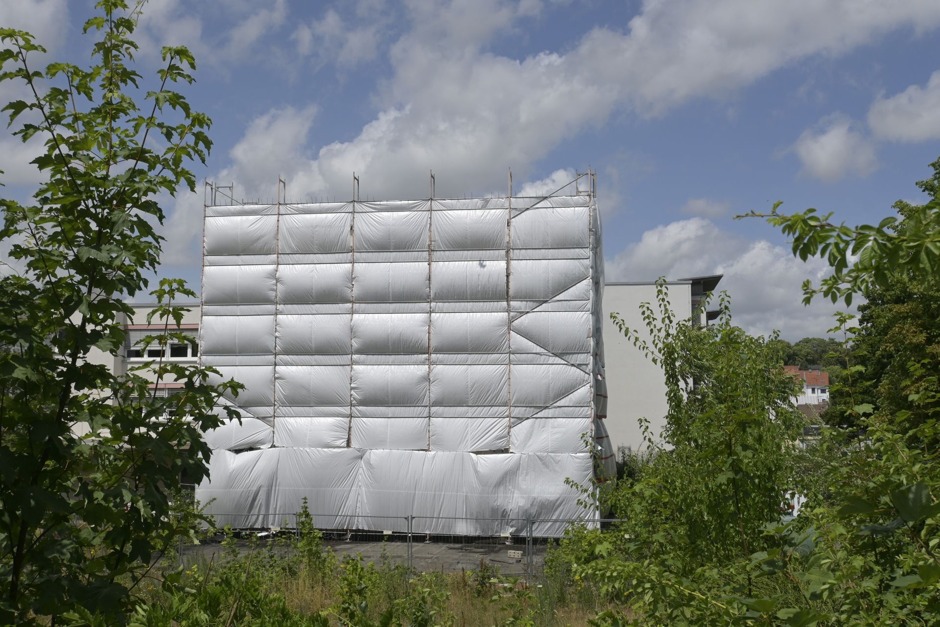 Façade du bâtiment recouverte de feuilles d'argent, arbres au premier plan, ciel nuageux.