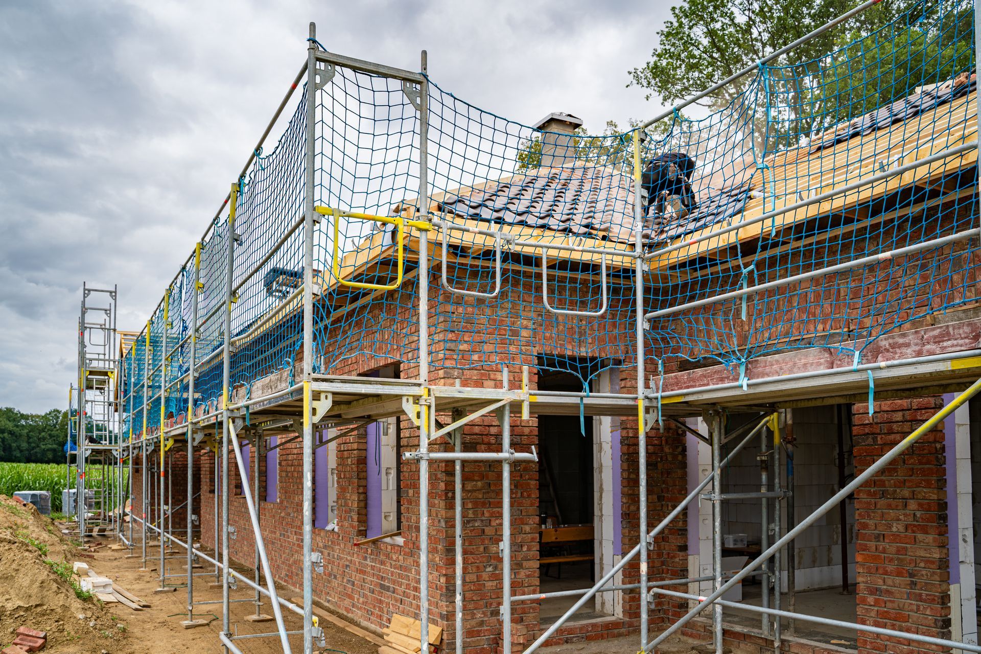 Chantier de construction avec échafaudages et filets de sécurité ; ouvrier sur le toit.