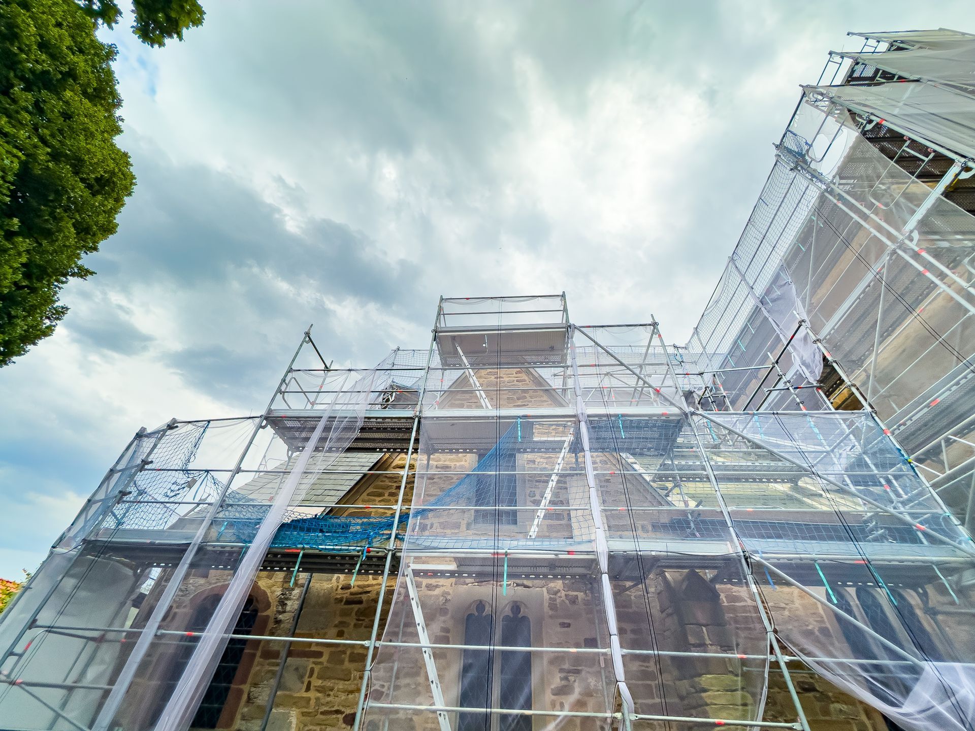 Église sous échafaudages, recouverte de filets, ciel nuageux.
